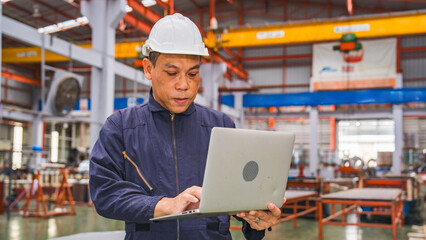 Professional Senior Asian technician engineer or inspector is using laptop in manufacturing factory planning production schedule, or doing a quality control checklist. Concept of technology in factory