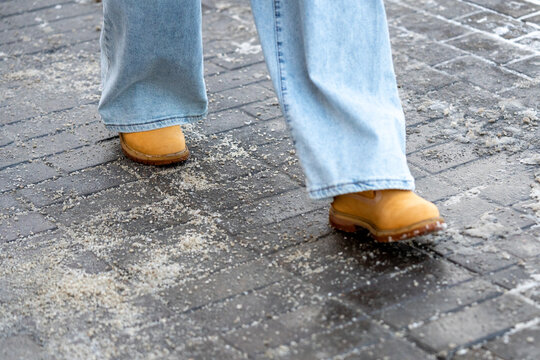 Anti-icing chemicals in winter season. Man walking on the street treated with technical salt or de-icing chemicals. Effective tool to fight ice on surfaces. Rock salt on road. 