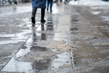 Anti-icing chemicals in winter season. People walking on the street treated with technical salt or de-icing chemicals. Effective tool to fight ice on surfaces. Rock salt on road. 