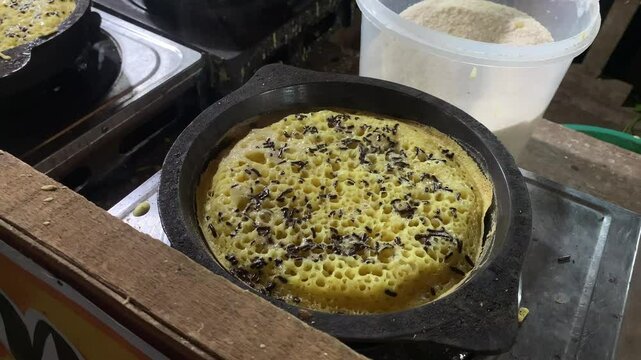 A freshly cooked "Terang Bulan" dessert in a traditional clay pan, topped with chocolate sprinkles.