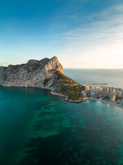 Aerial drone view of Calpe city. View of Ifach Mountain. Beautiful sunset colours reflecting on buildings and mountain. Travel destination in Alicante Province. Sunset point. 