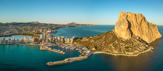 Aerial drone view of Calpe city. View of Ifach Mountain. Beautiful sunset colours reflecting on buildings and mountain. Travel destination in Alicante Province. Sunset point. 