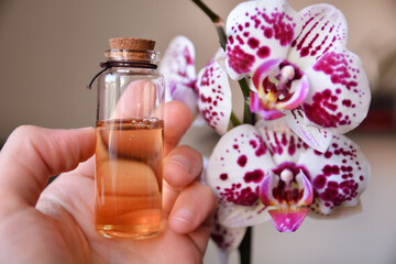 Hand holding a bottle of natural raw oil with exotic orchid flowers. Alternative medicine and organic skincare concept, close-up, selective focus