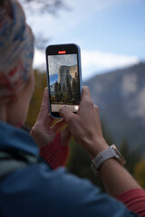Girl taking a foto of El Capitan rock in Yosemite National Park. Traveling and taking photos with the mobile phone. Phone screen closeup with the mountain.