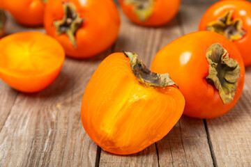 Persimmon on textured wooden background. Persimmon fruit. A piece of ripe, juicy, sweet persimmon fruit. Vegan. Orchard. Close-up. Space for text. Copy space.
