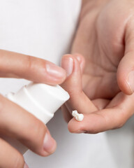 Woman squeezing hand cream on her finger and holding a cosmetic bottle in other hand, closeup