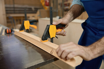 Carpenter fixing wooden plank on workbench with clamps at craft woodwork studio