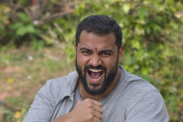 Fototapeta premium Portrait of a man expressing strong emotion in an outdoor setting with a blurred green background.