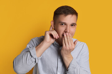 Man showing hand to ear gesture on orange background