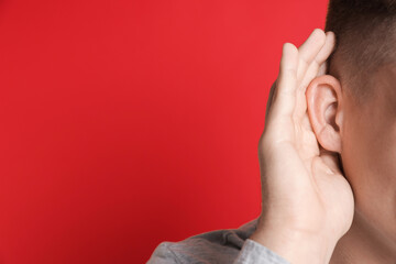 Man showing hand to ear gesture on red background, closeup. Space for text