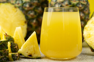 Pineapple juice in a glass among fresh pineapple fruit close-up.