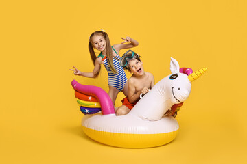 Happy little kids in beachwear with inflatable unicorn shaped ring on orange background © New Africa