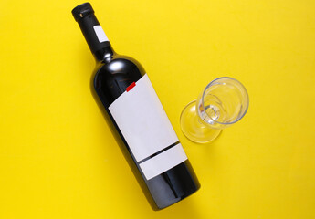 Red wine bottle with white blank label and glass on yellow background