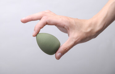 Female hand holding makeup sponge on gray background