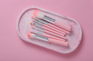 Set of makeup brushes in tray on pink background