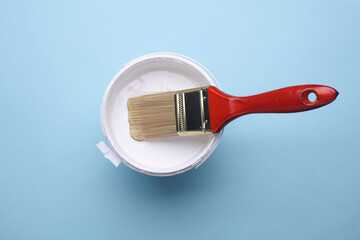 Paintbrush and can with white paint on blue background. Top view