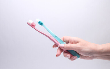 Female hand holding toothbrushes on gray background