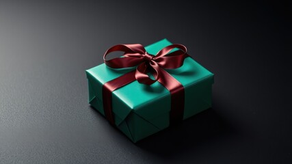 Obraz premium A teal gift box adorned with a luxurious burgundy bow, resting on a dark textured surface, creating a simple yet elegant scene.