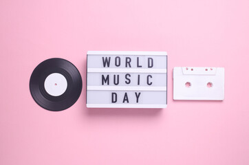 World music day text in light box and retro 80s audio cassette, vinyl record on pink background. Flat lay. Top view
