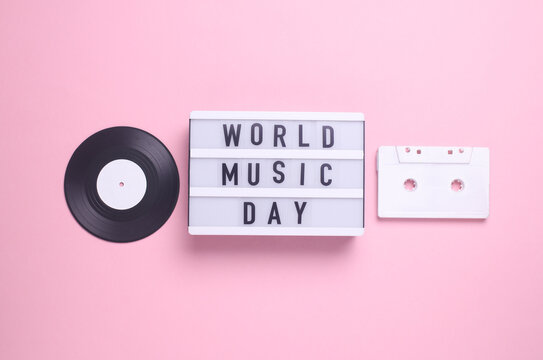 World music day text in light box and retro 80s audio cassette, vinyl record on pink background. Flat lay. Top view - Powered by Adobe