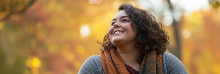 Fototapeta premium A young woman smiles softly, surrounded by warm autumn colors, reflecting peace and happiness in nature.