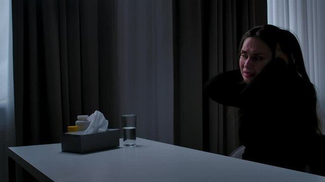 Woman suffering mental health issues, sitting at the table in front of camera, depressed expression, going mad, itching shaking head, side shot.