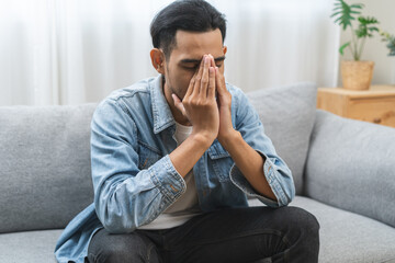 Sad upset, frustrated alone asian young man headache thinking about finance problem, difficulty, feeling failure and exhausted, suffering from loneliness sitting on couch at home. Grief sorrow, bad.