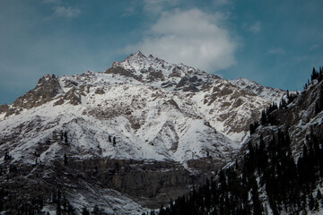 Obraz premium Sunlit Majestic Snow-Covered Mountain with Dark Green Trees