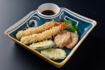 mixed tempura plate with fried shrimp and vegetables isolated on dark background 