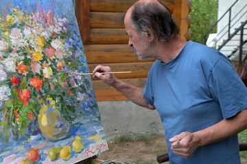 An artist with a brush in his hand paints a still life on canvas