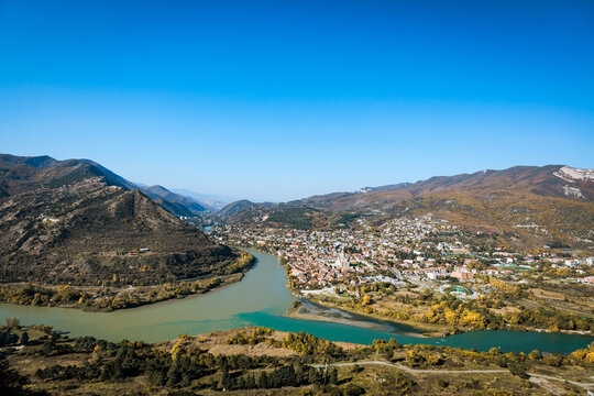 Confluence of Aragvi and Kura rivers with the historic town of Mtskheta, Georgia, seen from Jvari Monastery. Scenic aerial view of a cultural and natural landmark under a clear blue sky