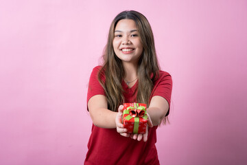 A cheerful young woman with long brown hair and light skin, wearing a red T-shirt, holds a small...