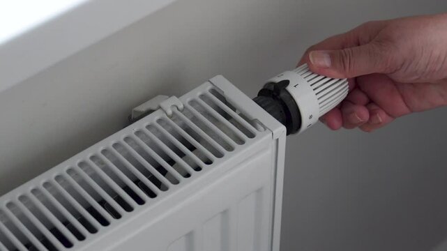 Close up female hands checking temperature radiator and adjusting thermostat knob to increase or decrease heat output, energy efficiency and comfort. Heating period in house. High payments and savings