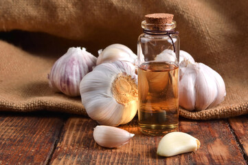 Raw and ripe garlic with garlic oil in a glass bottle on a wooden table. Natural remedy and organic concept. Close-up, garlic background