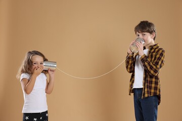 Boy and girl talking on tin can telephone against beige background