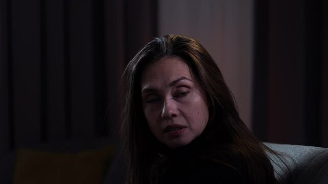 Woman suffering mental health issues, sitting on the sofa covered in blanket, depressed expression talking to herself, going crazy, close up.