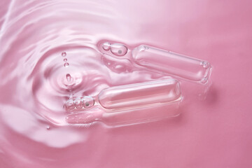 Ampoules in water on a pink background.