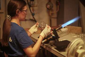 A young girl blows glass toys for the Christmas tree. Glass blower at a Christmas tree decorations...