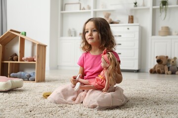 Cute little girl playing with her doll on floor at home
