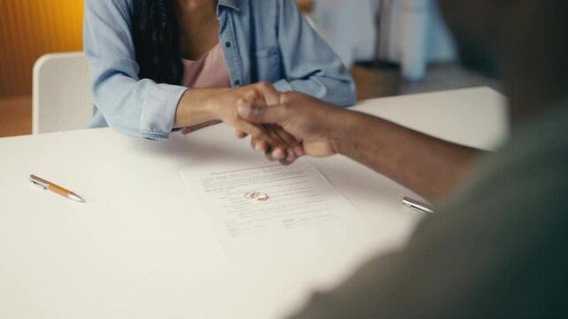 Black couple places wedding rings on divorce papers while shaking hands, closure