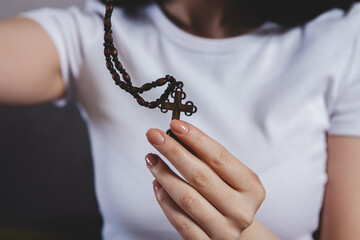 female praying with rosary on wooden background.