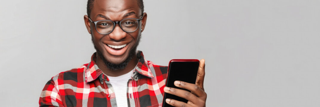 Young african american man smiling broadly while holding smartphone on neutral background