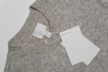 A beige wool sweater with a round neckline, featuring an empty inner label and two blank tags...