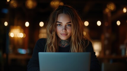 A young woman with a tattooed neck uses her laptop in a warmly lit, cozy environment, surrounded by blurred lights, evoking a sense of creativity and focus.