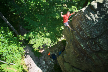Aerial view of male rock climber ascending rugged limestone cliff with harness and rope for safety....