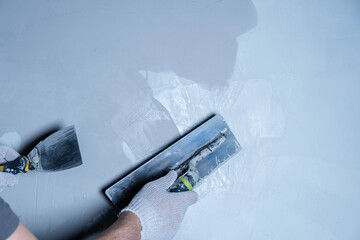 A person uses a trowel to apply epoxy adhesive on a smooth surface in a workshop.