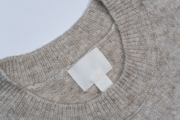 Beige wool sweater with an empty inner label on the neck. The soft knitted fabric and blank tag provide a perfect background for customization, allowing space for branding, size, or care instructions.