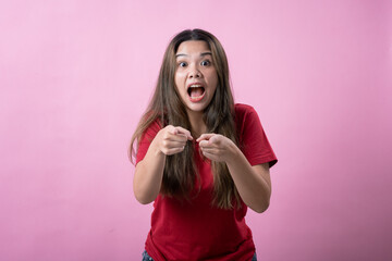 Excited Asian woman in red shirt with long brown hair points forward enthusiastically with wide...