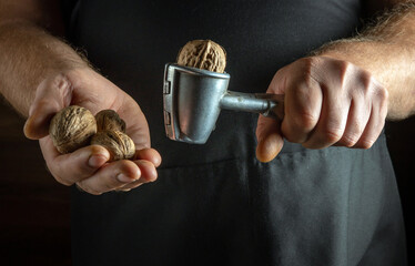 A person skillfully uses a nutcracker to open walnuts held in one hand, showcasing the joy of...