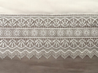 Close up of table runner with white floral lace, white ornamental braids and brown base background....